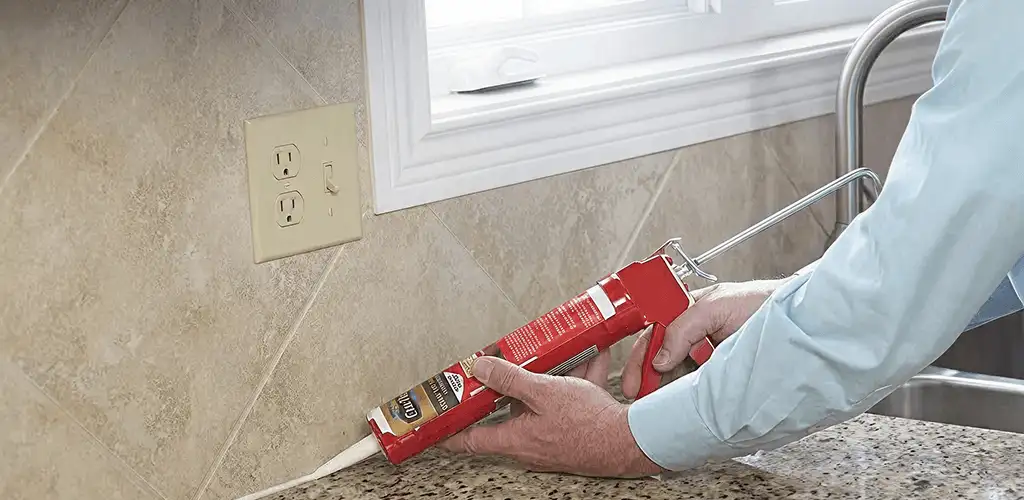 Handyman applying caulk along a kitchen backsplash and countertop seam in Colorado Springs, CO